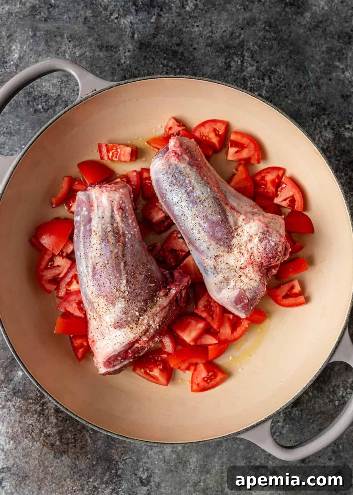 overhead process shot: seasoned lamb shanks in dutch oven on top of diced tomatoes