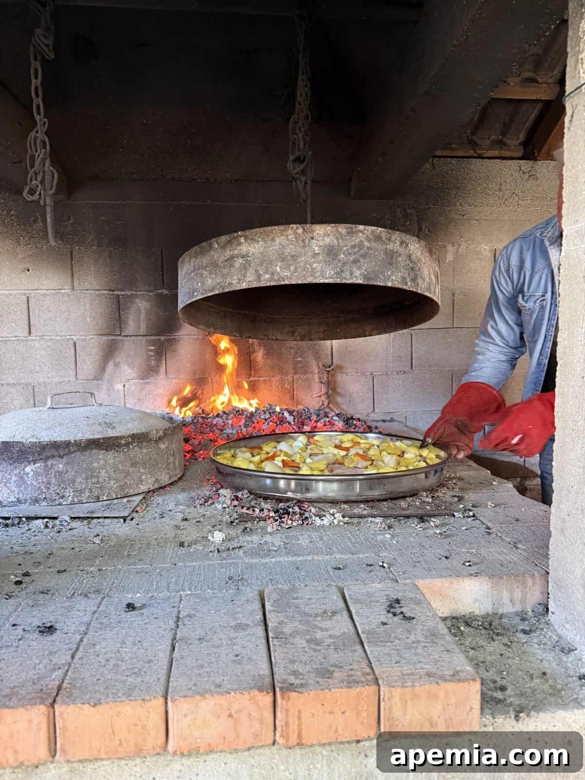 sideview process shot: peka ingredients in pan under domed iron lid attached to chain