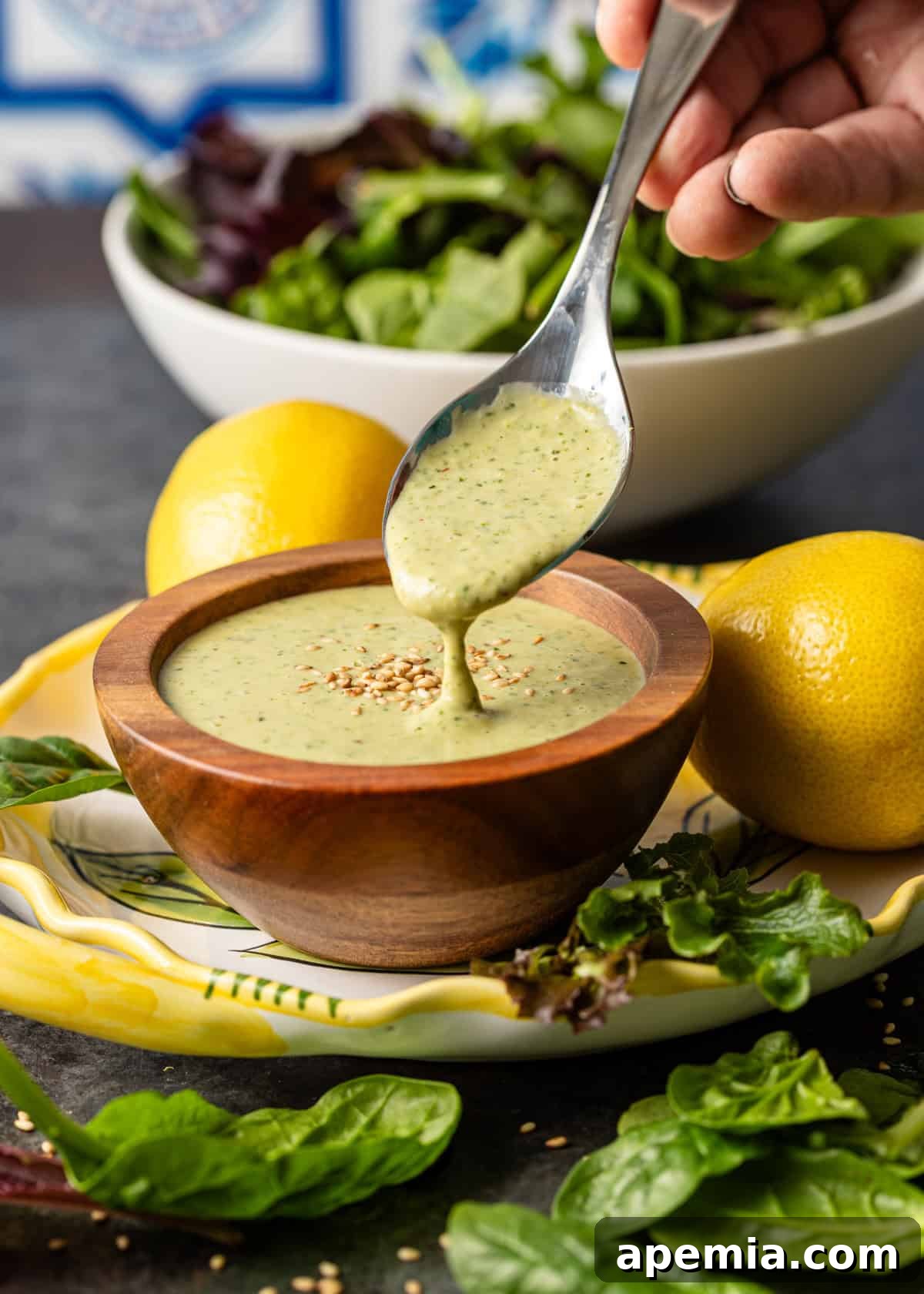 Closeup side view of a spoonful of creamy lemon tahini dressing held over a wooden bowl, ready to be served, showcasing its rich texture.