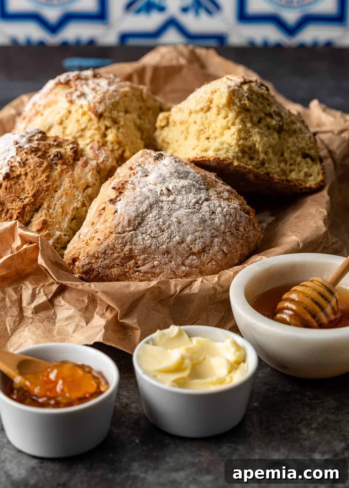 Closeup side view of a round Irish soda bread in a rustic basket, with various spreads beautifully arranged on the side, inviting you to enjoy.