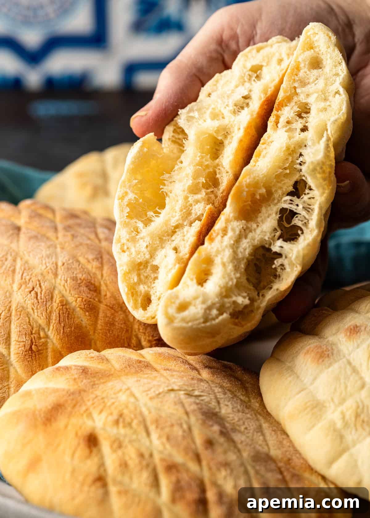 Classic Balkan Flatbread Lepinja 3 closeup side view: hand holding sliced lepinja over bowl of bread