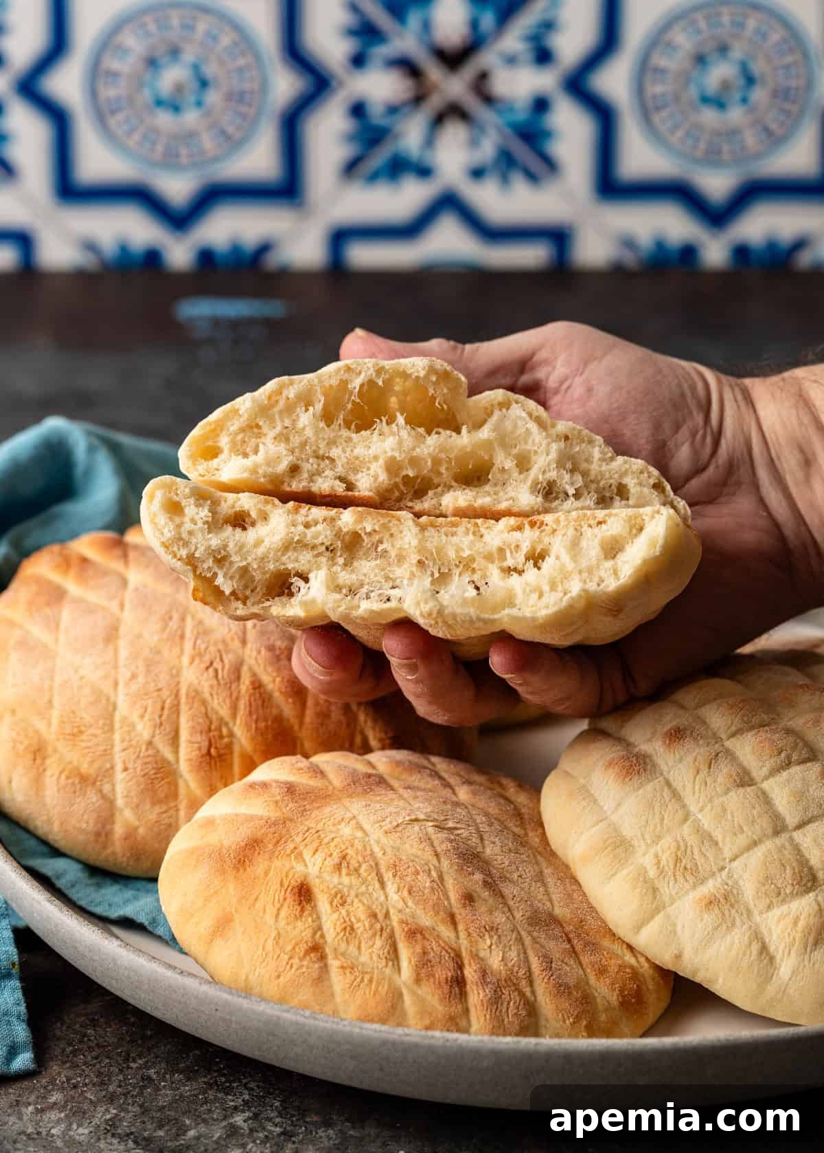 Classic Balkan Flatbread Lepinja 24 closeup side view: hand holding sliced Balkan flatbread over top of bowl of bread