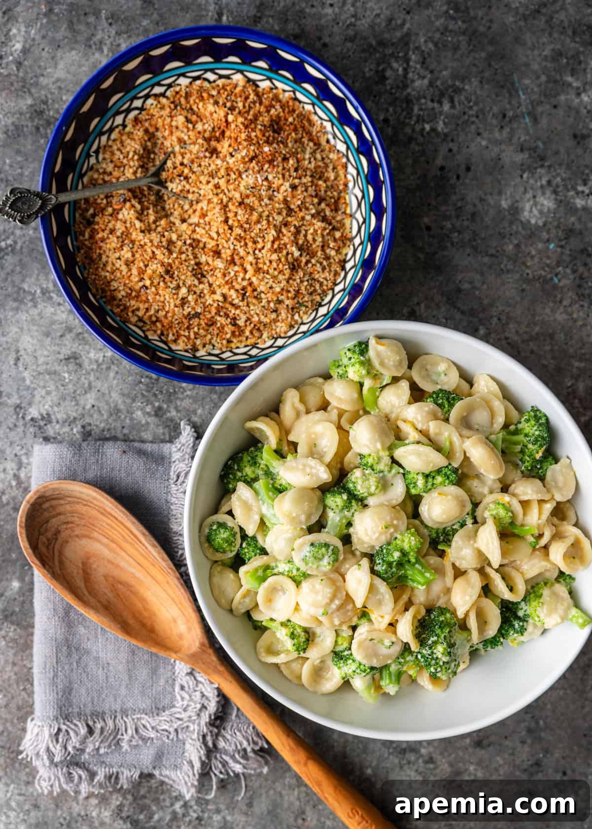 overhead: white bowl of broccoli pasta with another bowl of toasted breadcrumbs