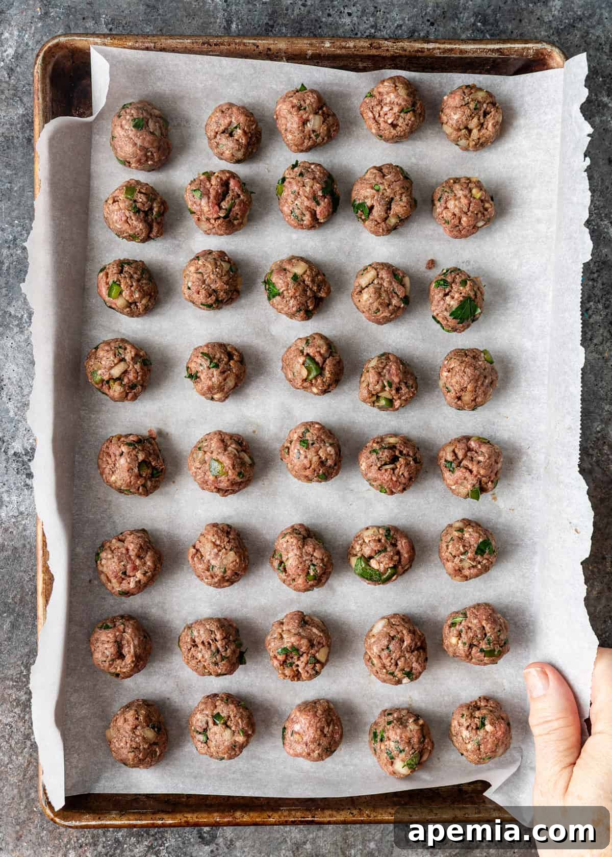 Overhead process shot of perfectly rolled tiny meatballs arranged on a parchment-lined baking sheet, ready for the stew.