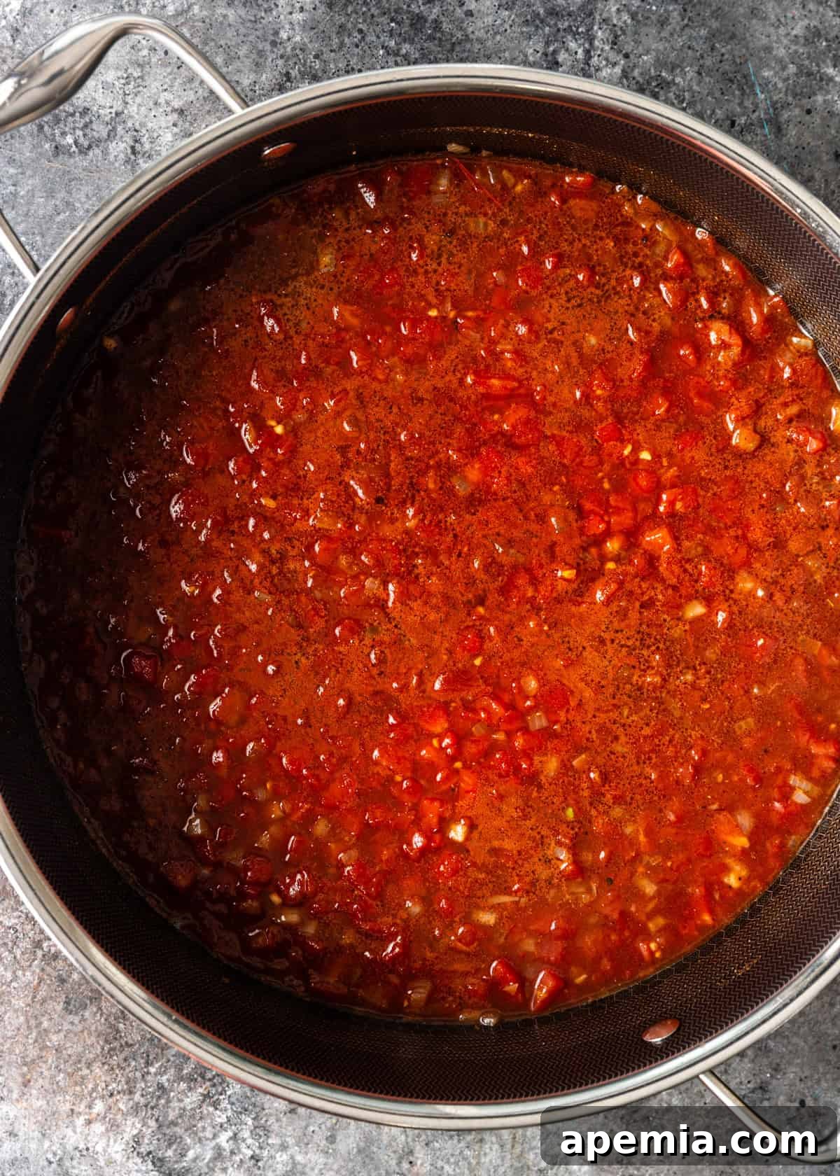 Overhead process shot illustrating the vibrant tomato mixture simmering in a pot, forming the base of the stew.