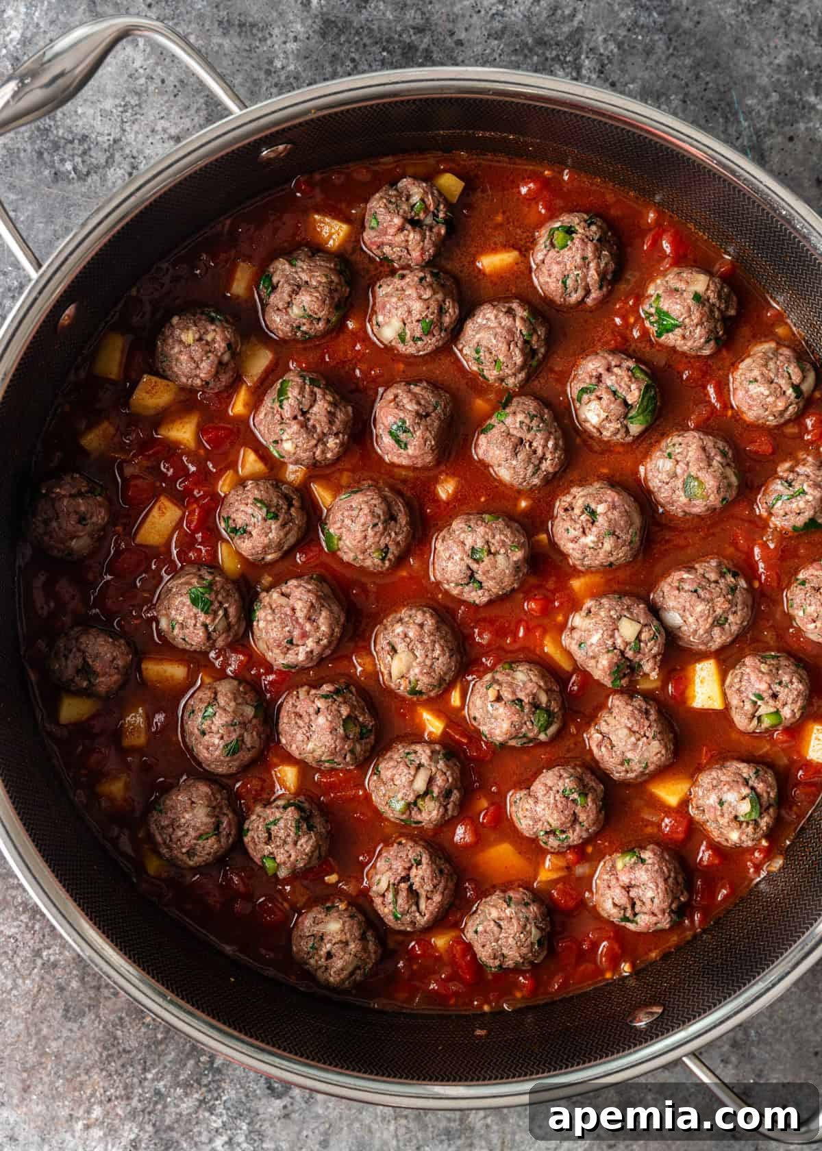 Overhead process shot showing the small, tender rolled meatballs carefully placed on top of the simmering tomato mixture in the pot.