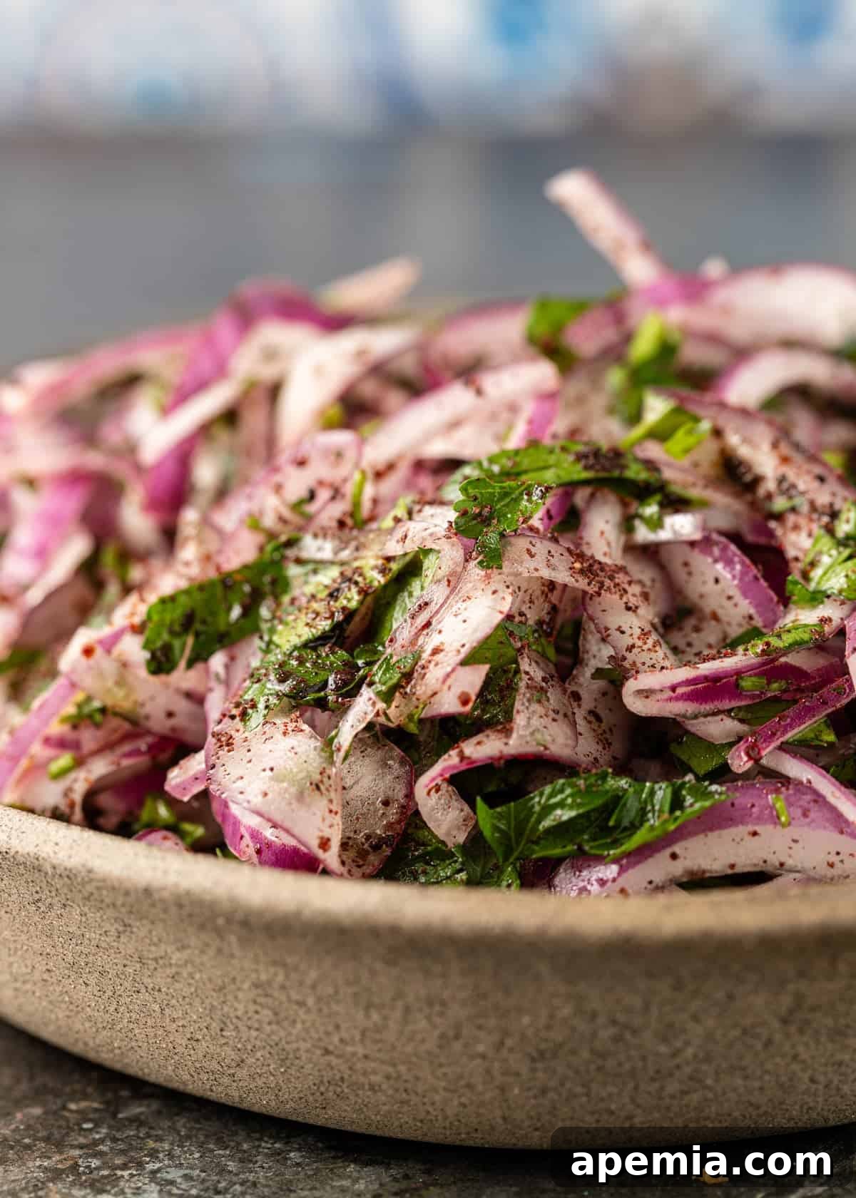 Overhead view of a wooden bowl filled with bright red sumac onions and fresh herbs.