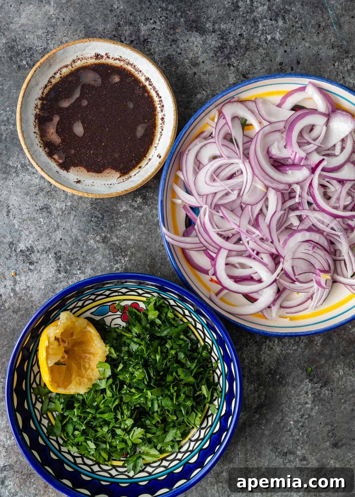 Overhead view of thinly sliced red onion, lemon wedges, and sumac spice, ready for mixing.