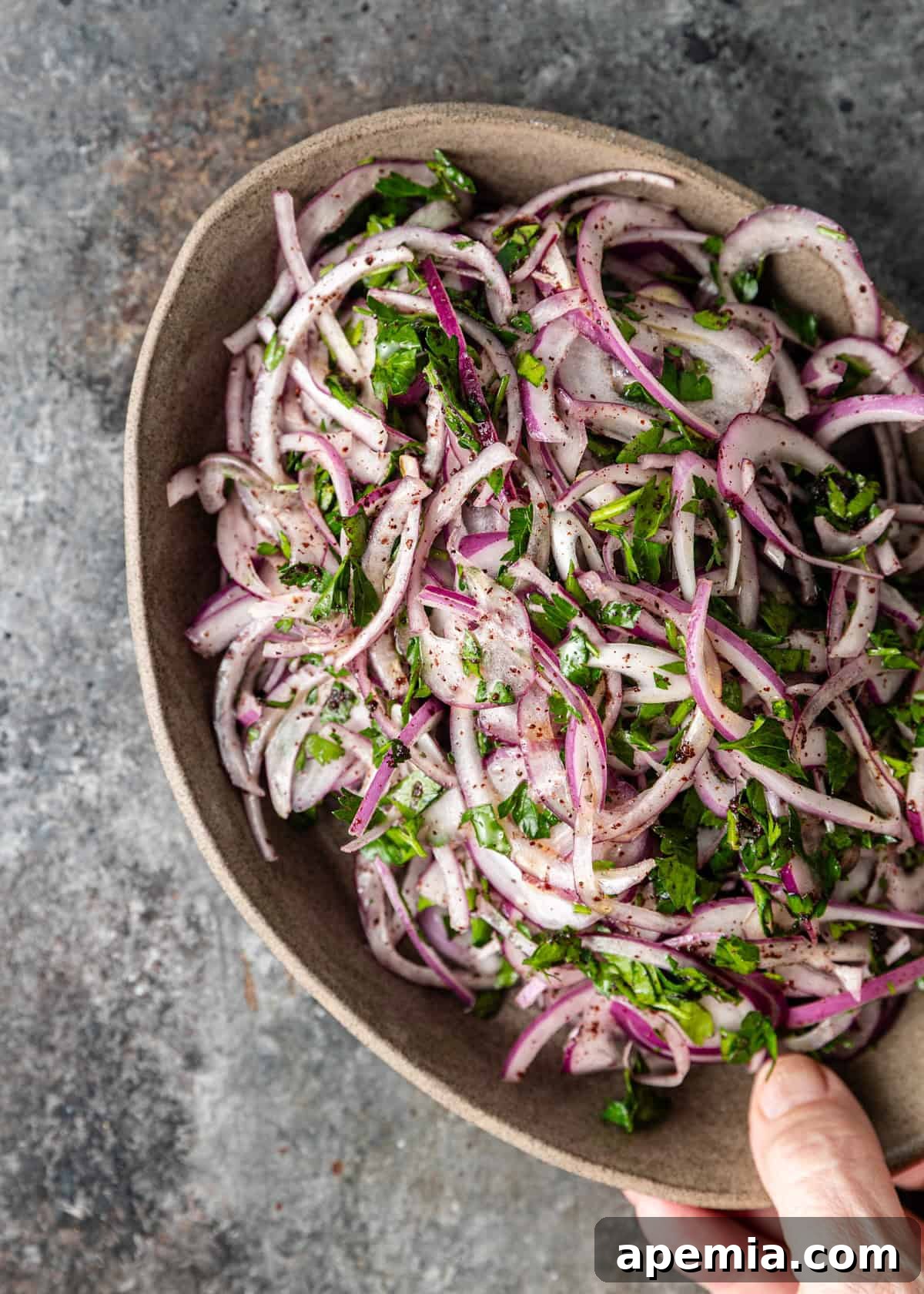 A hand gently tossing sumac onions in a bowl, showing the vibrant color and fresh herbs.