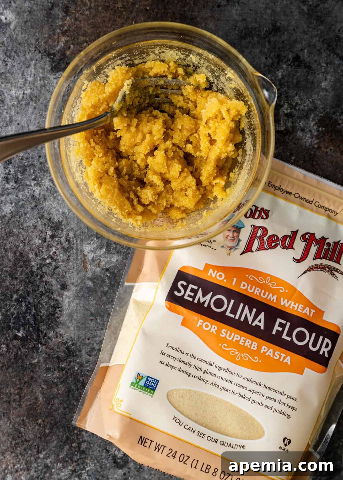 Process shot: a measuring cup of fine semolina being mixed with olive oil in a bowl.