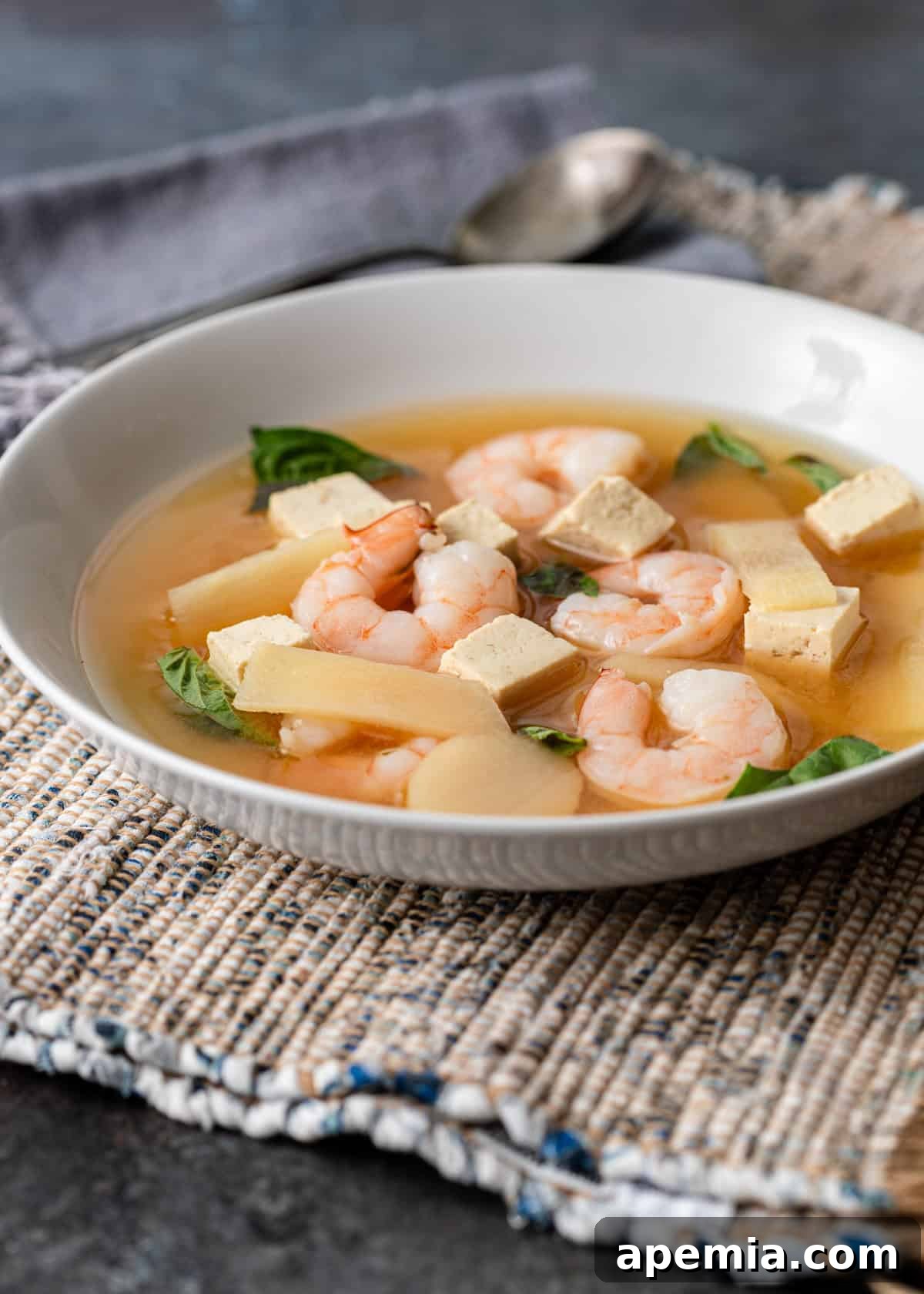 closeup side view: white bowl of shrimp soup with spoon off to side
