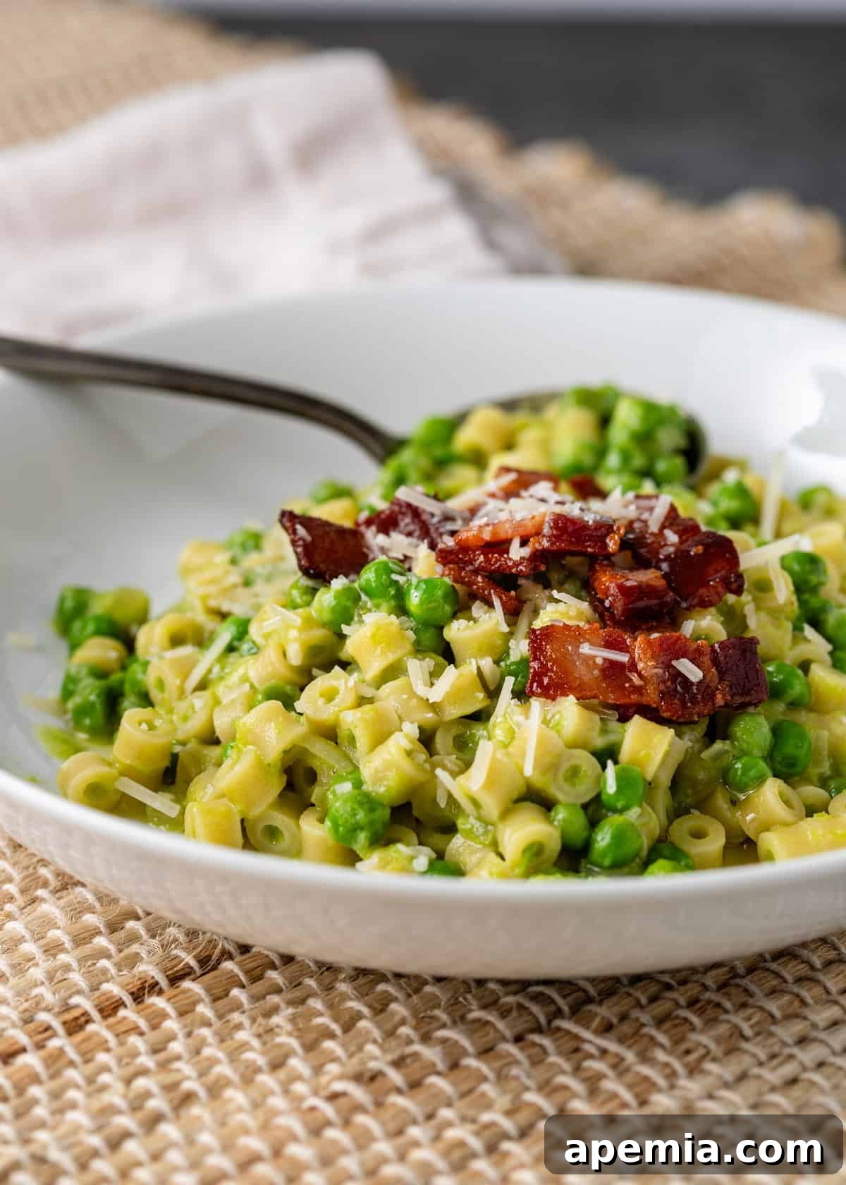 closeup side view: ready to eat pasta with peas on white plate with spoon