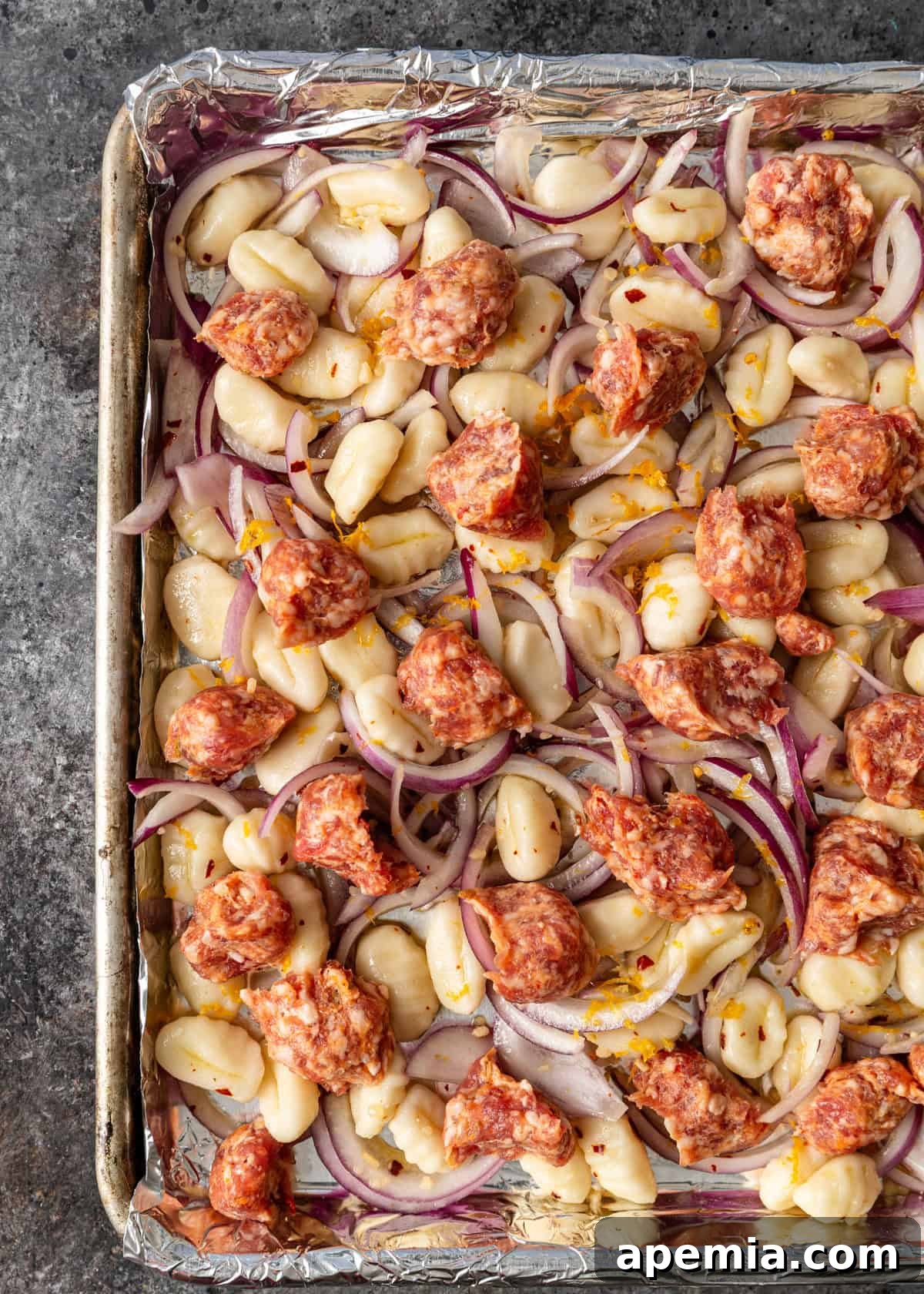 overhead process shot: crumbled sausage added to sliced red onions and gnocchi mixture on baking sheet