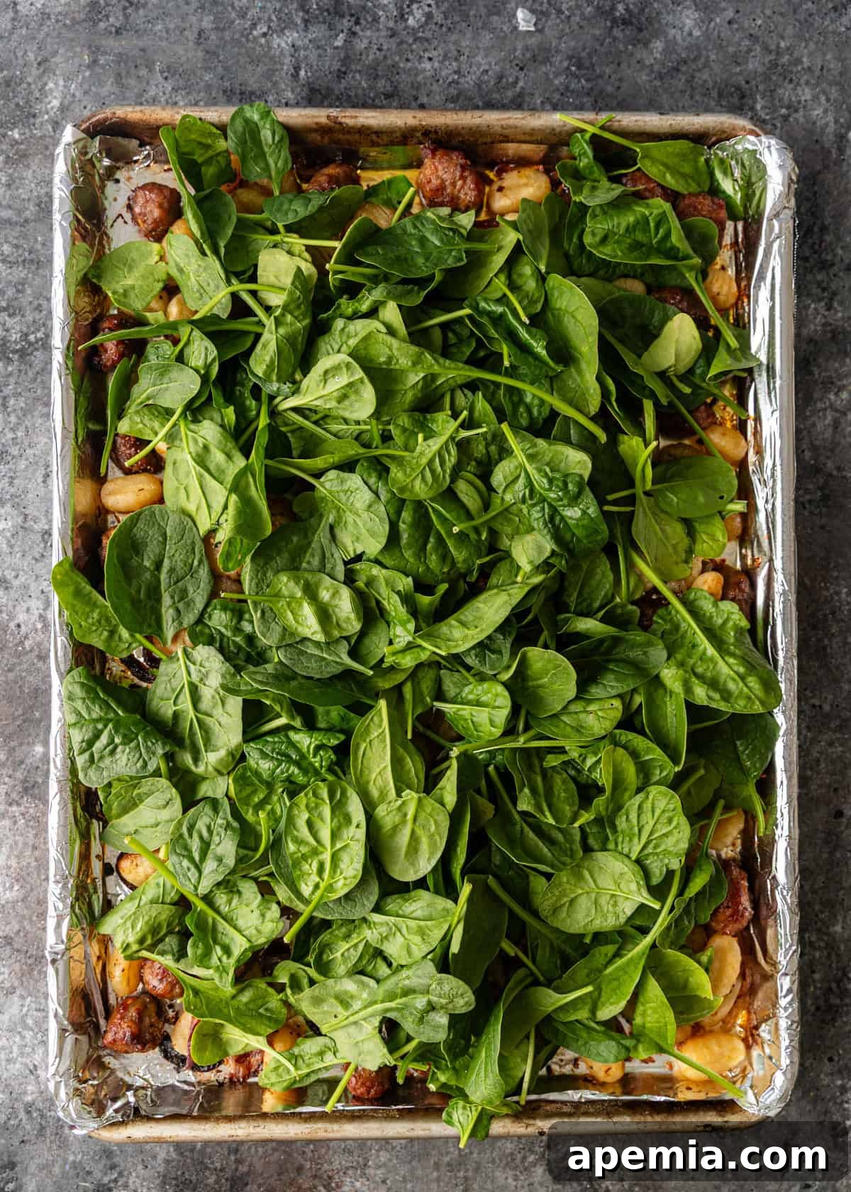 overhead: fresh spinach leaves added to foil lined baking sheet