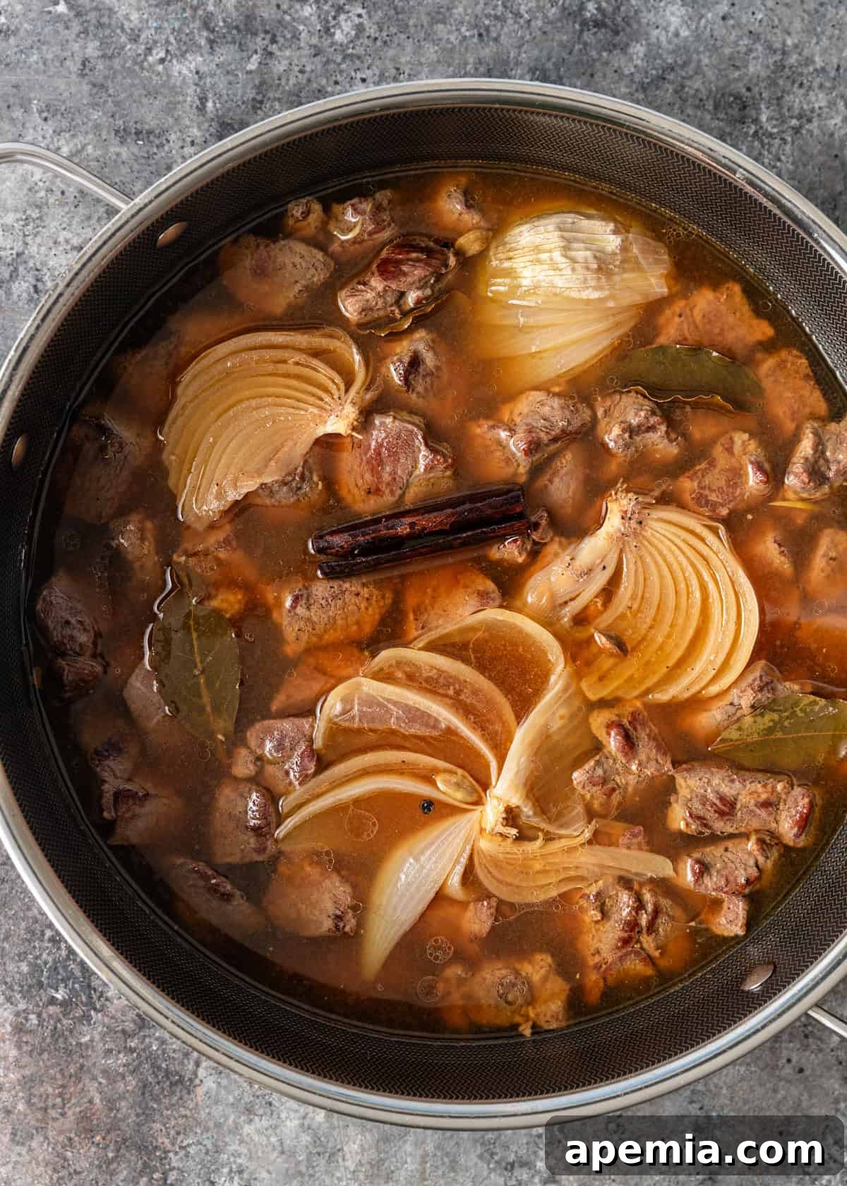 overhead process shot: soaked lamb in water, cardamom, bay leaves, cinnamon, peppercorns, and onion