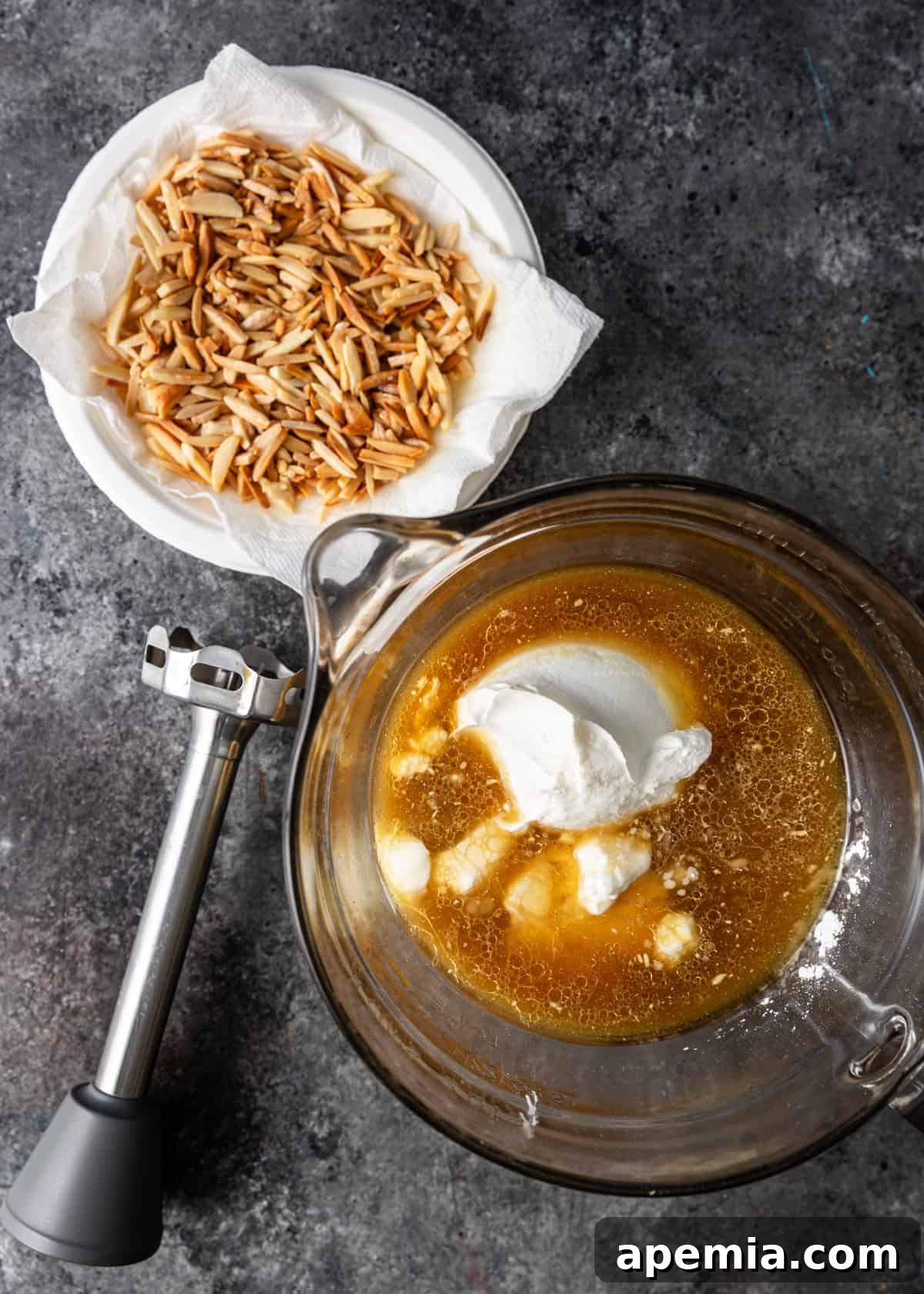 overhead process shot: ingredients to make this jameed sauce in measuring cup with hand mixer and bowl of diced almonds on side