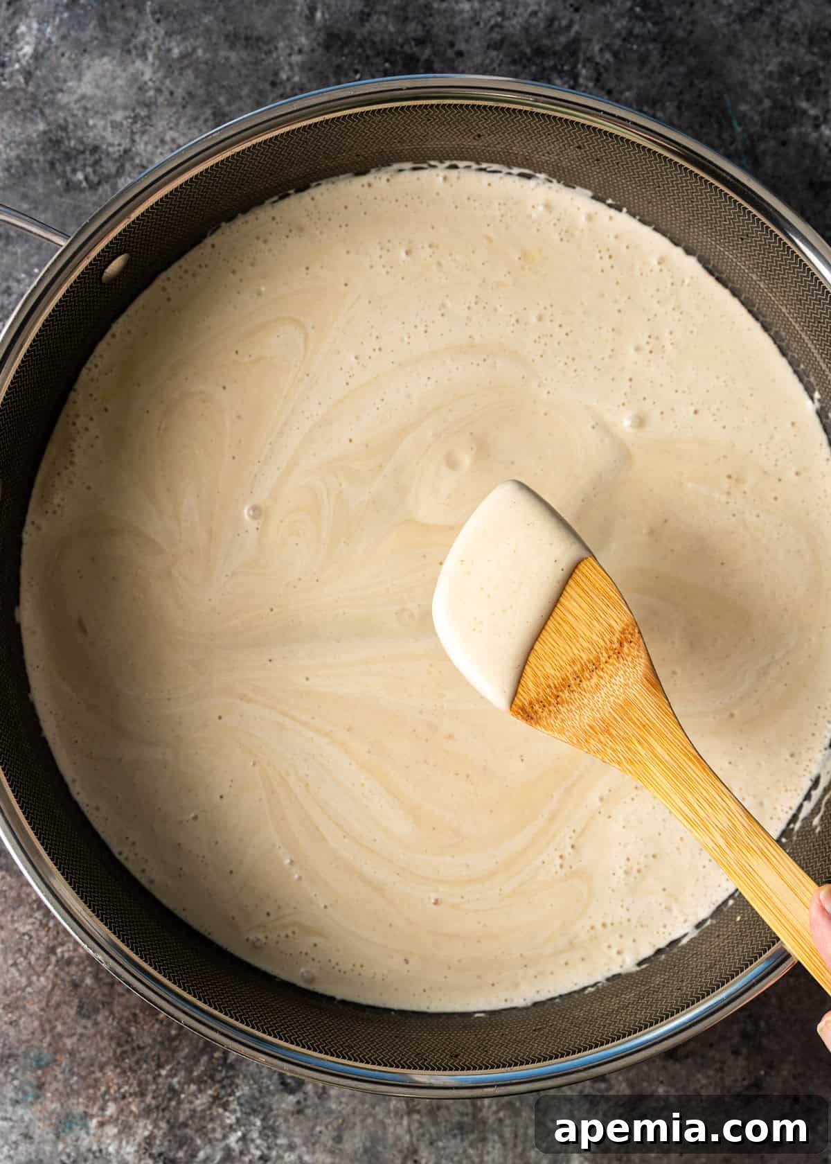 overhead process shot: jameed mixture cooking in Dutch oven pot with hand holding spatula 