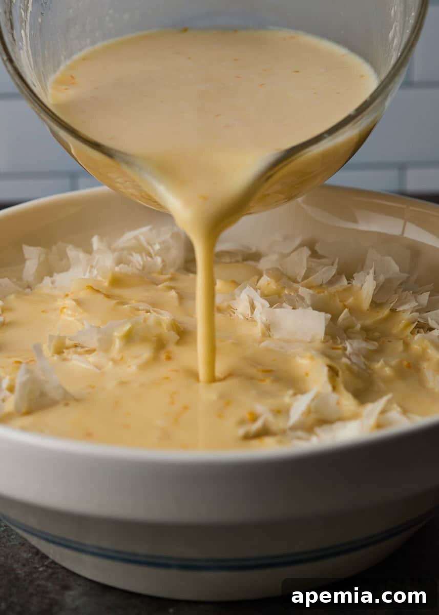 closeup side view: measuring cup with sauce being poured onto torn pieces of phyllo dough