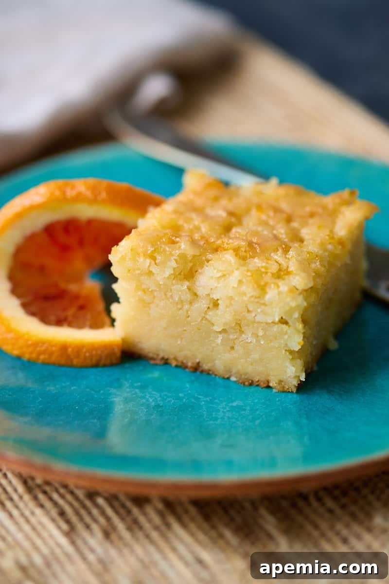 closeup side view: slice of portokalopita on blue plate with fork and slice of orange