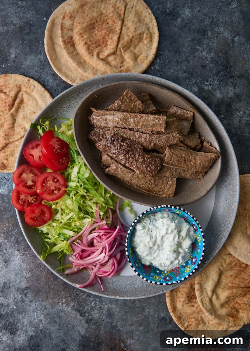 overhead: bowl of sliced meat on plate with lettuce, tomatoes, onions, and small bowl of tzatziki sauce