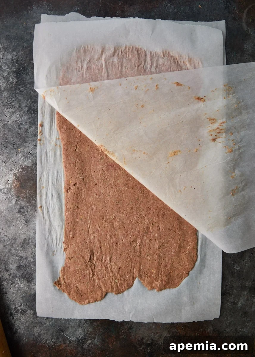 overhead process shot: meat rolled between two parchment papers and the top being lifted off