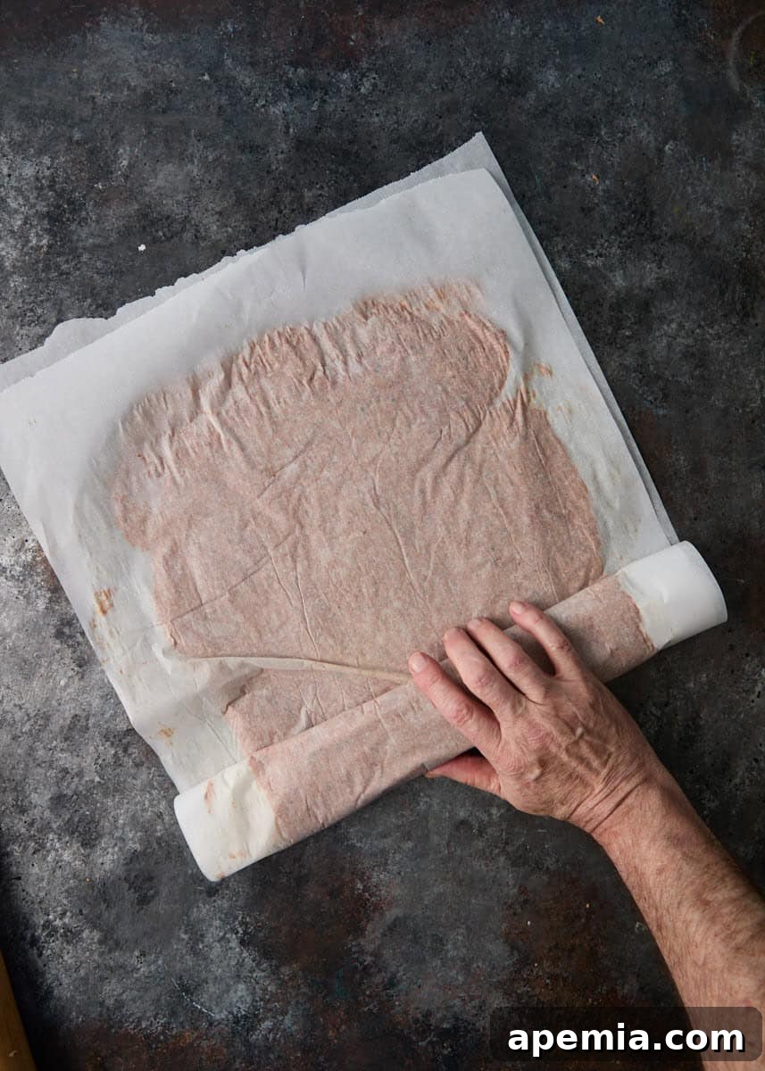 overhead process shot: hand rolling parchment paper with meat rolled between