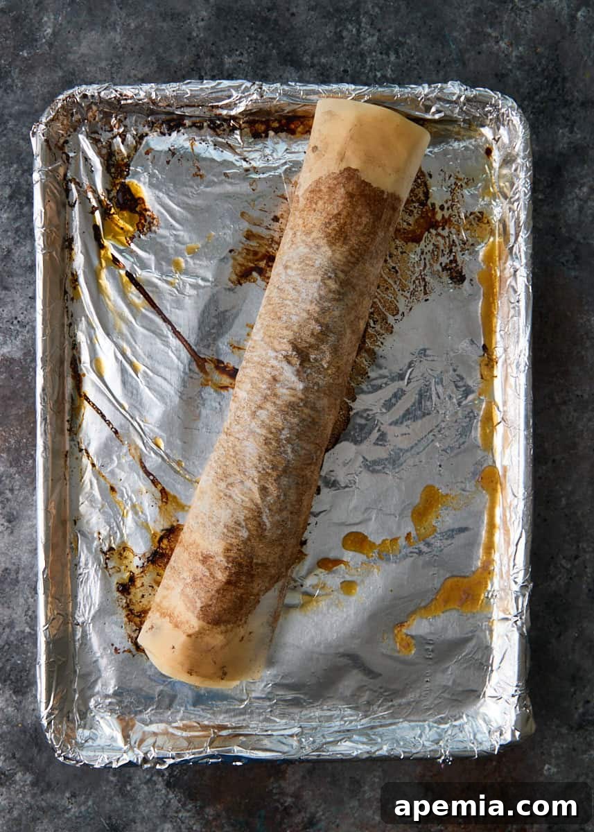 overhead process shot: cooked rolled meat in parchment paper on top of foil on sheet pan