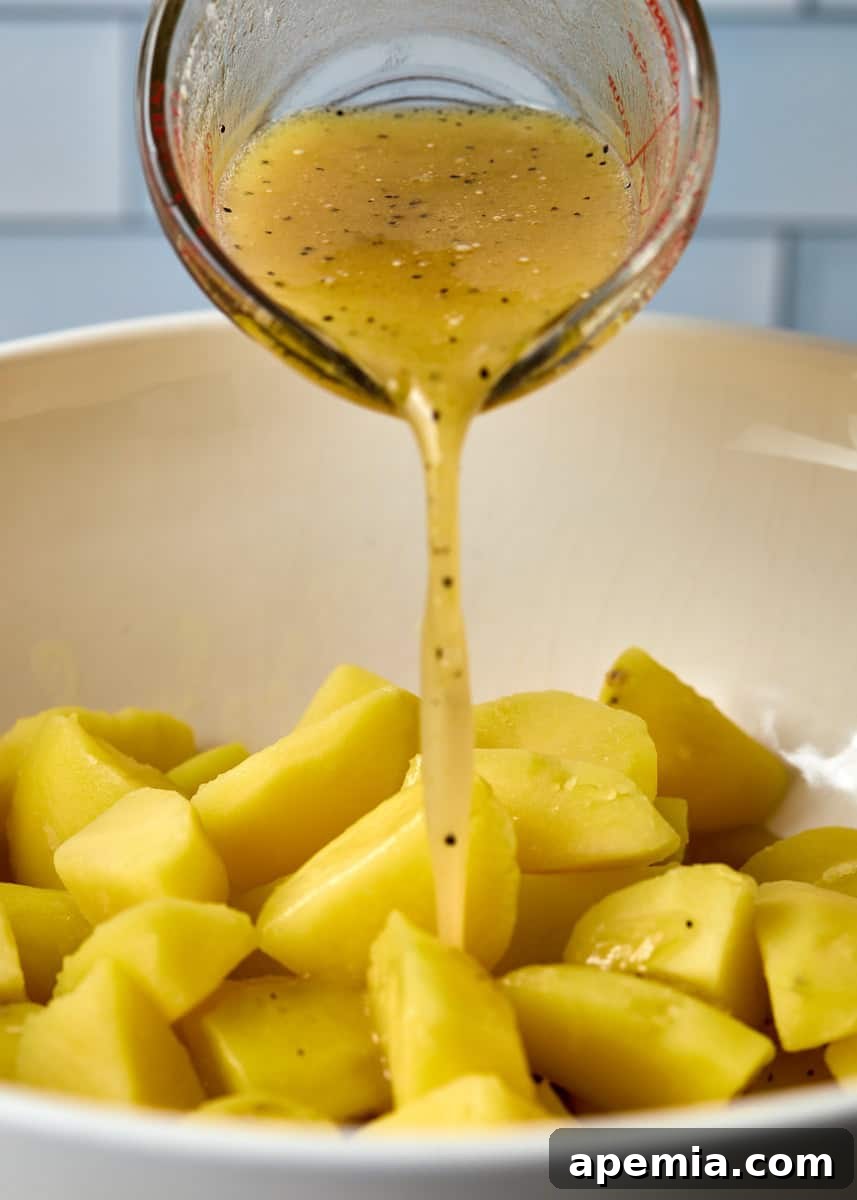 side view process shot: dressing being poured from measuring cup into bowl of cut potatoes