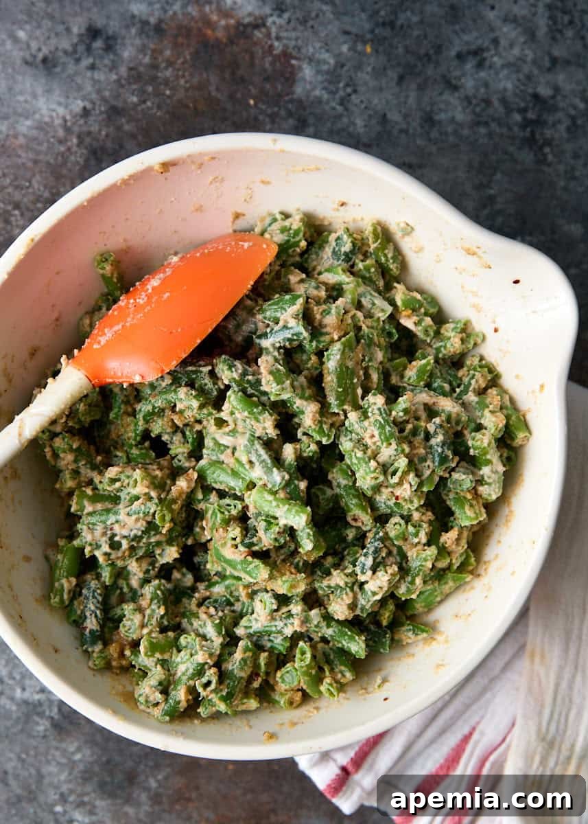 overhead: bowl of green beans and sauce mixed together with spatula